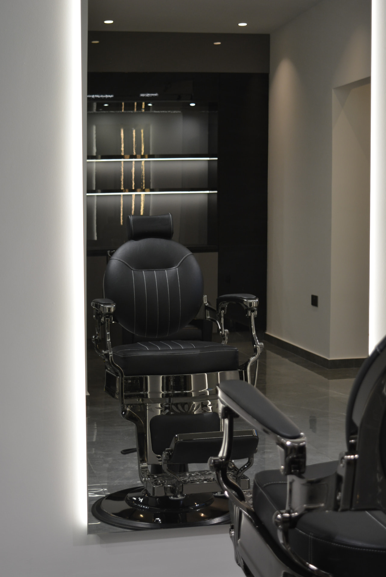 Black edition barber chair reflected in the backlit mirror at Primera Barbershop